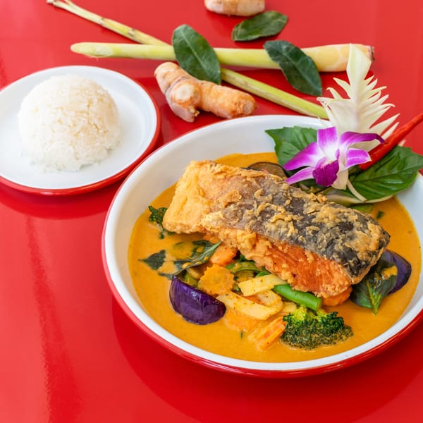 Thai red curry with crispy salmon, vegetables, and rice, garnished with an orchid.