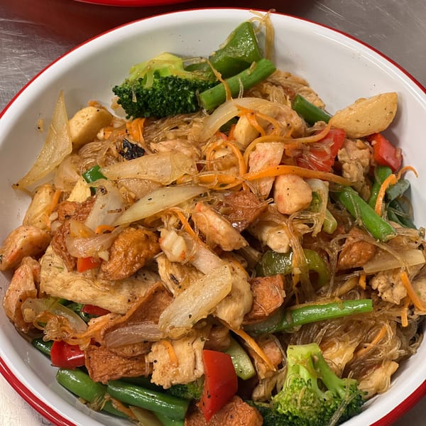 A close-up of a Thai glass noodle dish with chicken, vegetables, and tofu in a white bowl.