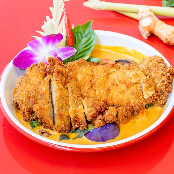 Crispy duck in red curry sauce with vegetables, garnished with an orchid and chili.