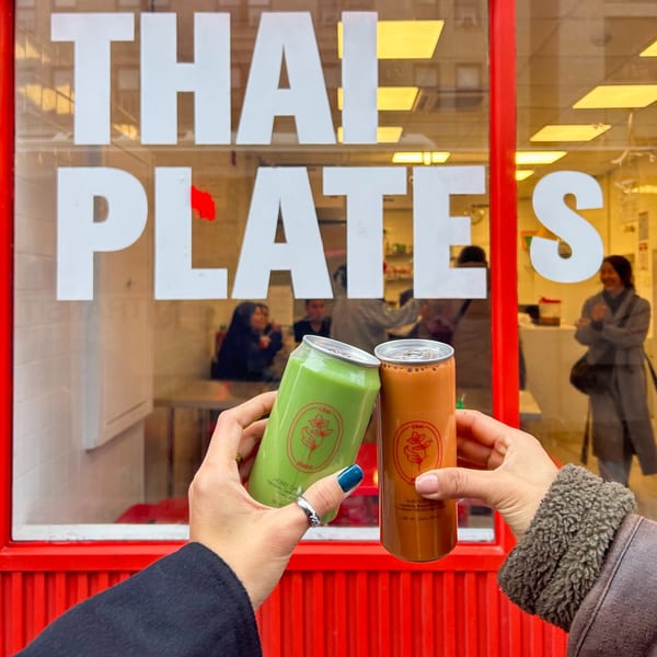 Two hands holding green and orange Thai iced tea cans in front of the Thai Plates restaurant.