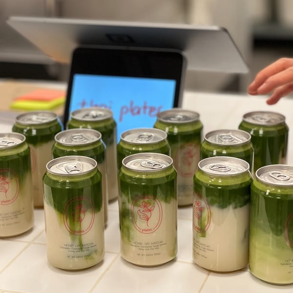 Rows of Thai Plates' Honey Oat Matcha drinks in cans with a tablet displaying the restaurant name.